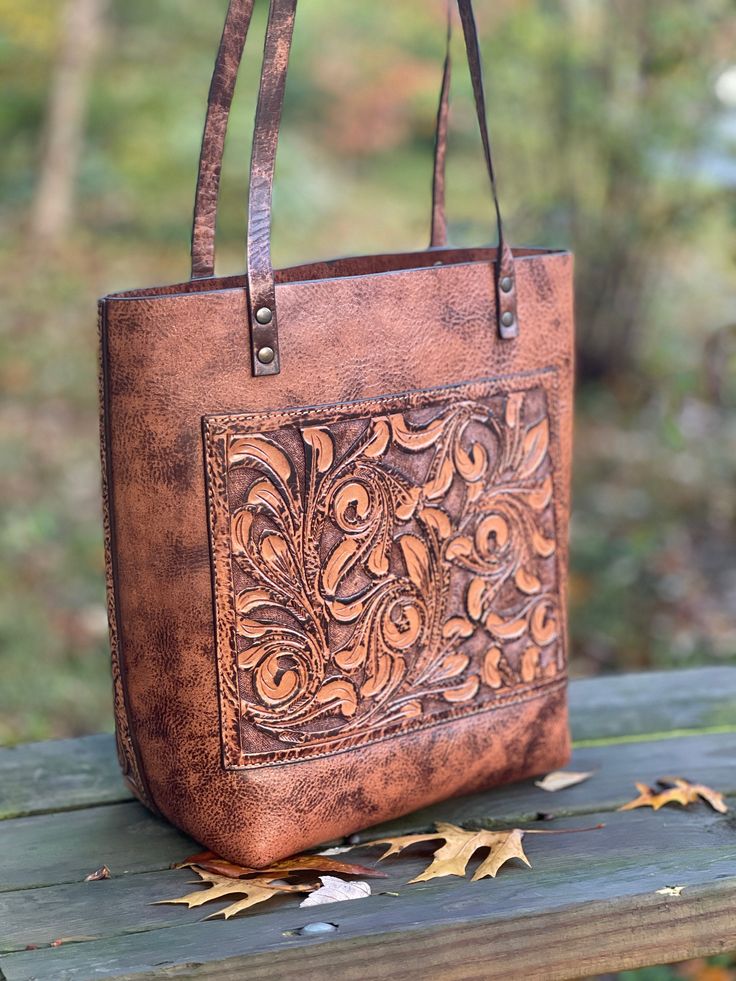 "Introducing our exquisite Hand-Tooled Leather Tote Bag ELODIA, a timeless piece of art crafted from premium quality leather. Each tote bag is carefully hand-made using traditional leather crafting techniques and tools, resulting in a one-of-a-kind piece with intricate designs and patterns. This tote bag features spacious compartments for your daily essentials and comfortable carrying. The interior is leather to keep your items safe and protected. The bag is also designed with a sturdy base, mak Elegant Embossed Rectangular Bag, Elegant Embossed Tote Bag, Elegant Embossed Bags For Daily Use, Elegant Embossed Rectangular Shoulder Bag, Elegant Rectangular Embossed Shoulder Bag, Elegant Embossed Bag, Hand Tooled Satchel Bag As Gift, Hand Tooled Satchel Bag For Gifts, Hand Tooled Shoulder Bag As Gift