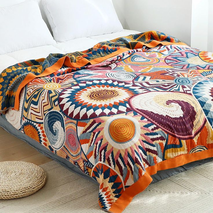 a bed covered in an orange, blue and white comforter next to a wicker basket