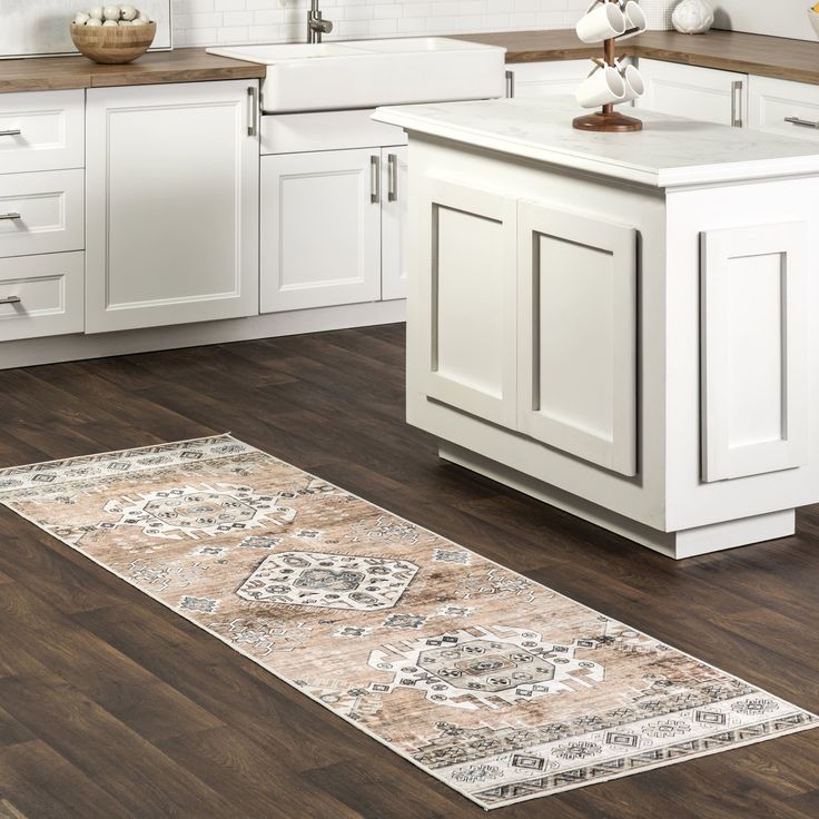 a kitchen with white cabinets and wood flooring is pictured in this image, the area rug has an ornate design on it