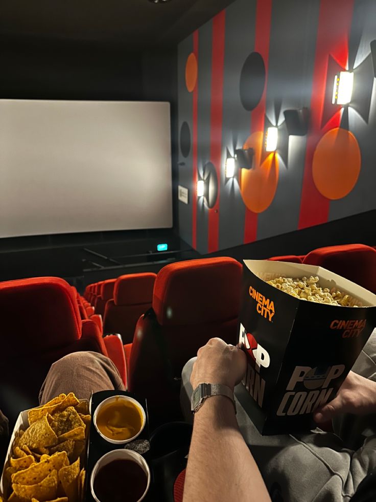 a man sitting in front of a movie screen holding a box of popcorn