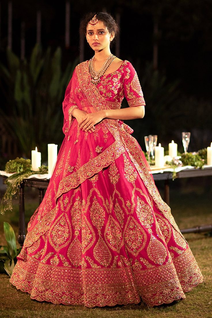 a woman in a red and gold wedding gown standing on the grass with candles behind her