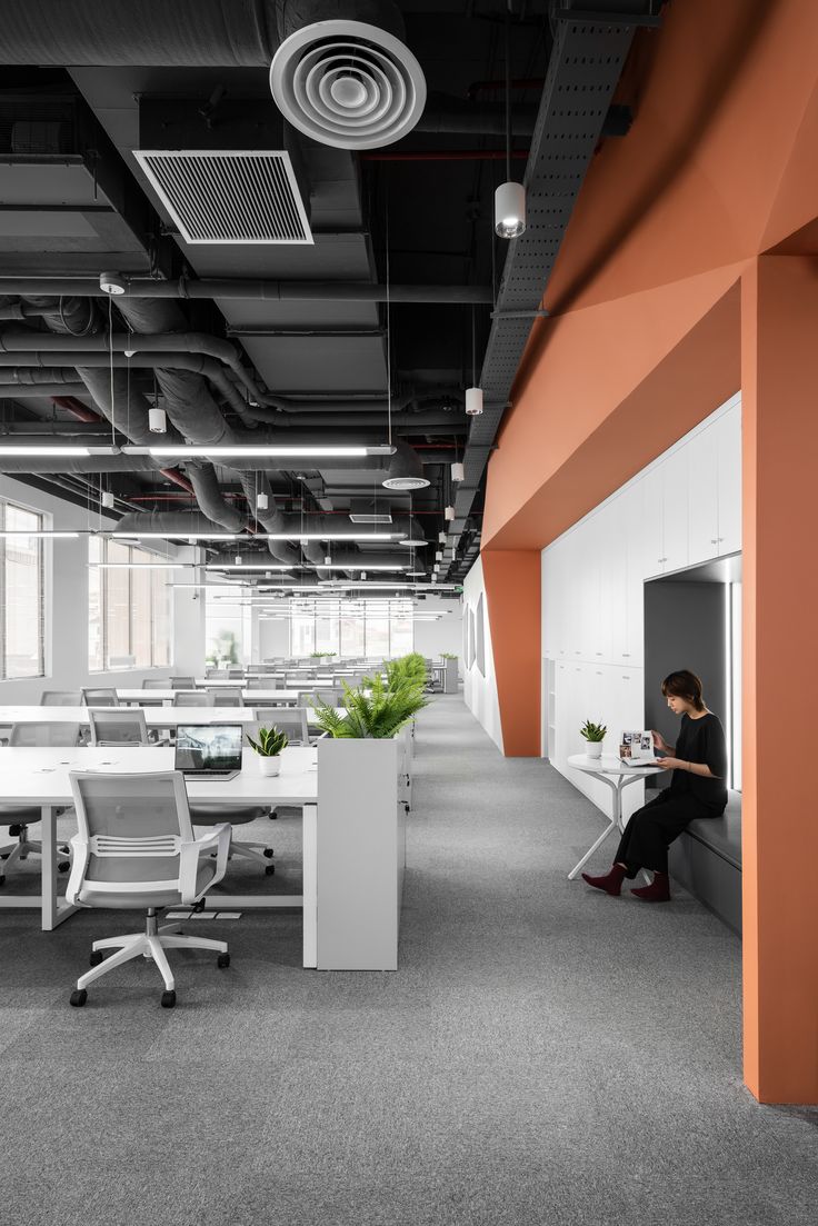 a person sitting at a desk in an office with orange walls and white chairs around it