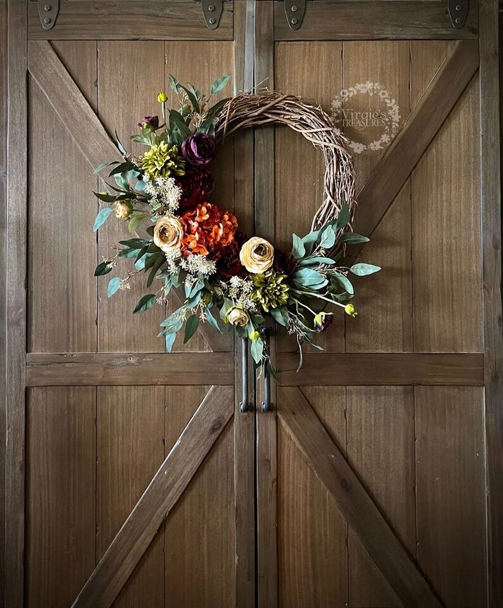 a wreath on the front door of a house with flowers and greenery around it