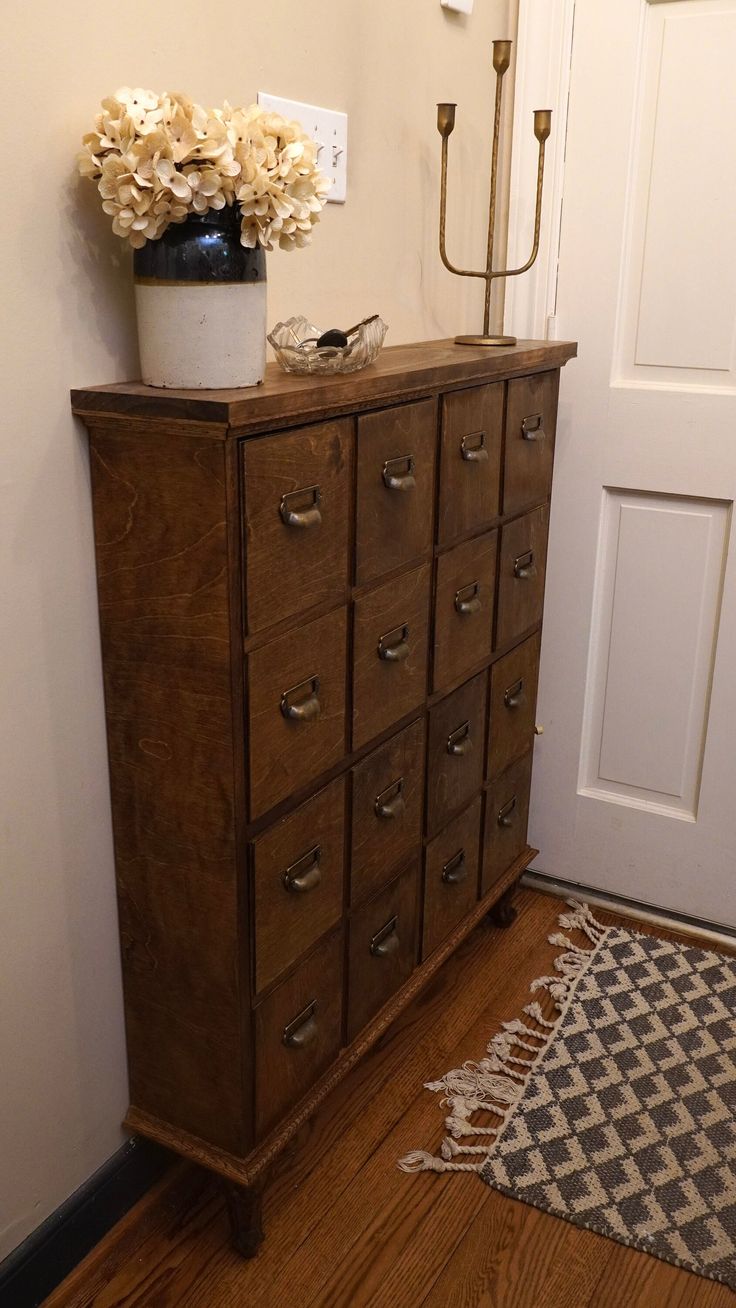 a wooden dresser with flowers in a vase on top and a rug underneath it next to a door