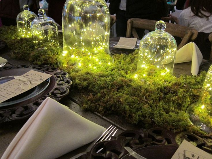 the table is set with glass cloches covered in moss and lite - up fairy lights