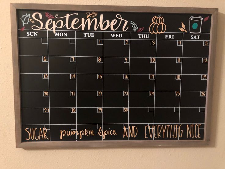 a chalkboard calendar hanging on the wall next to a coffee cup and pumpkins