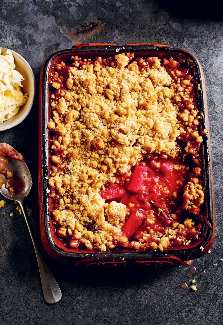 a casserole dish with crumbled toppings next to a bowl of ice cream