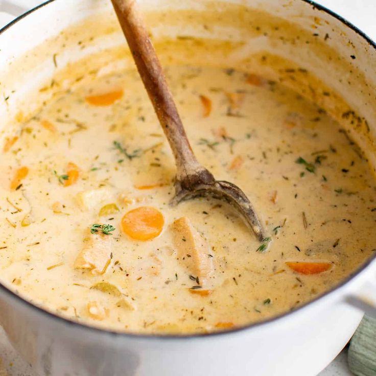 a wooden spoon in a pot filled with chicken chowder soup on a white surface