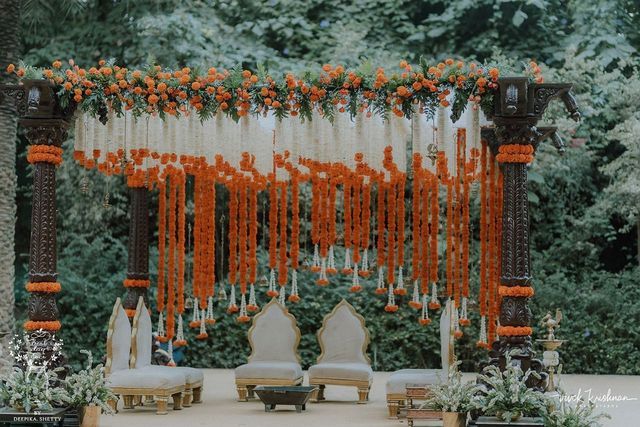 an outdoor wedding setup with orange and white flowers hanging from the ceiling, surrounded by greenery