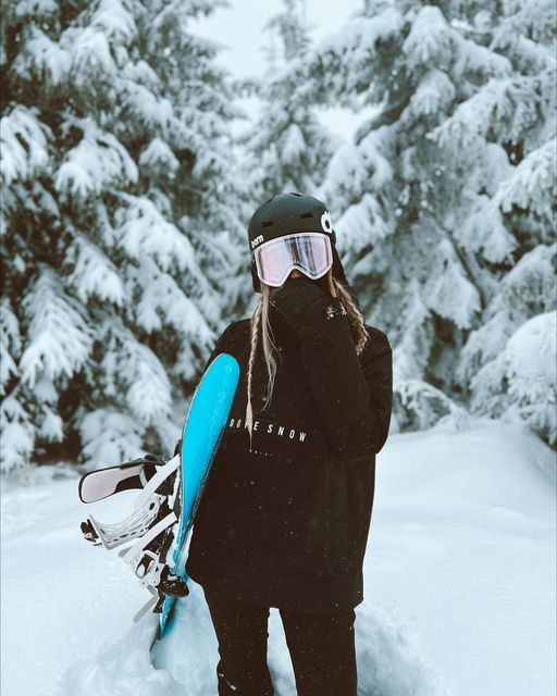 a person standing in the snow with skis on their shoulders and wearing goggles