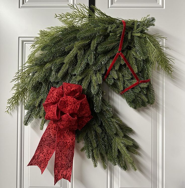 a christmas wreath hanging on a door with a red bow and green pine needles attached to it