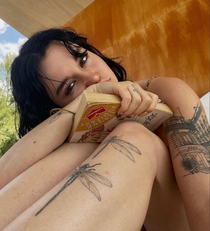 a woman with tattoos on her legs is laying down and holding a block of cheese