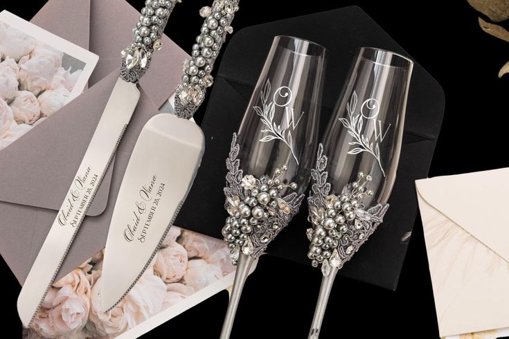 two champagne flutes sitting on top of a table next to an envelope and flower arrangement