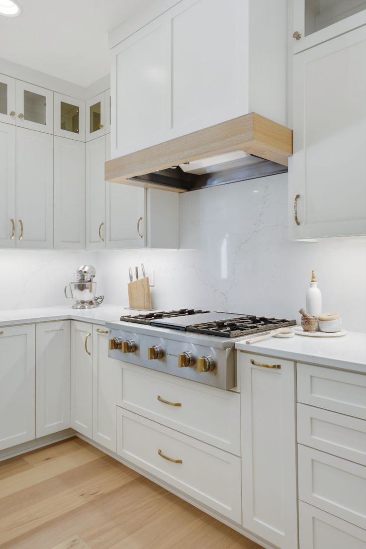 a kitchen with white cabinets and gold pulls on the stove top, which is surrounded by wood flooring