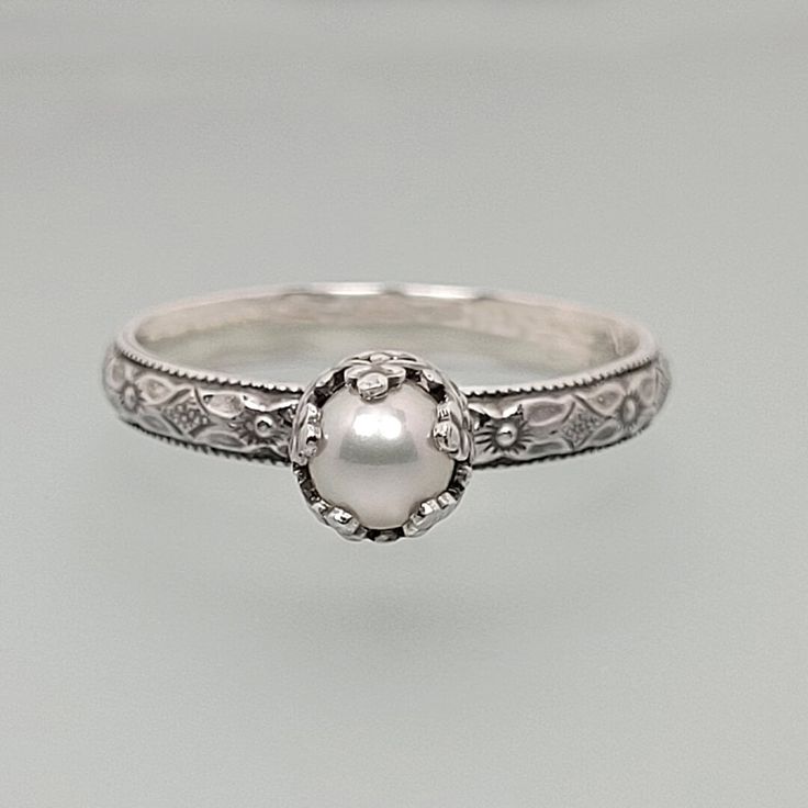 an antique style pearl ring with filigrees on the sides and engraving detailing