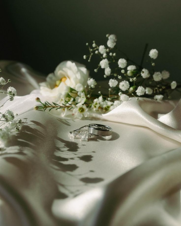 two wedding rings sitting on top of a white cloth next to flowers and greenery