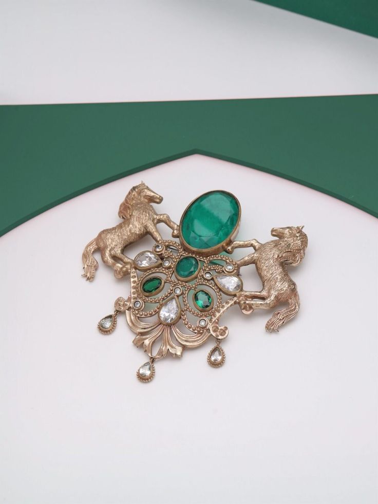 The "Roshan-e-Sawaar Brooch" is an enchanting ode to untamed beauty. This captivating accessory showcases two intricately designed galloping horses, adorned with four stunning green gemstones that exude elegance and vitality. The Glitter Horse Brooch captures the untamed grace and boundless energy of these majestic creatures, empowering every modern individual to embrace their inner strength and free spirit. With its dazzling beauty and symbolic significance, this brooch is the perfect statement Luxury Green Brooches For Wedding, Antique Wedding Brooch With Intricate Design, Victorian Wedding Brooches With Intricate Design, Gold Brooches With Intricate Design For Wedding, Luxury Wedding Brooch Jewelry, Heirloom Wedding Brooches With Intricate Design, Antique Gold Brooches For Wedding, Traditional Formal Brooch With Intricate Design, Victorian Gold Brooch For Wedding