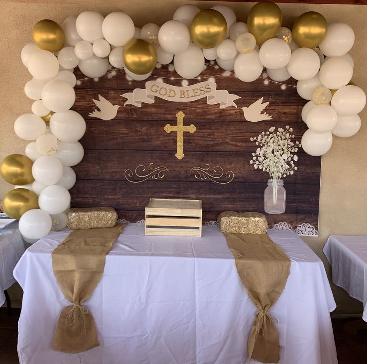 a table topped with white and gold balloons next to a wooden sign that says christ