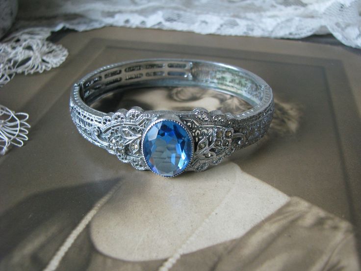 A beautiful Art Deco blue and clear paste floral filigree bangle bracelet. It measures 3/4'' at widest Measures 2 3/8'' x 2'' across the inside, and is 6 3/4'' along the inside. in very good condition with some graying and yellowing to the clear paste stones Heirloom Jeweled Bracelets For Wedding, Heirloom Jeweled Wedding Bracelets, Heirloom Style Adjustable Cuff Bracelet For Weddings, Antique Adjustable Wedding Bracelets, Antique Adjustable Bracelets For Wedding, Blue Round Cuff Bracelet For Formal Occasions, Filigree Bracelet For Wedding, Vintage Oval Bangle For Wedding, Sapphire Filigree Jewelry For Wedding