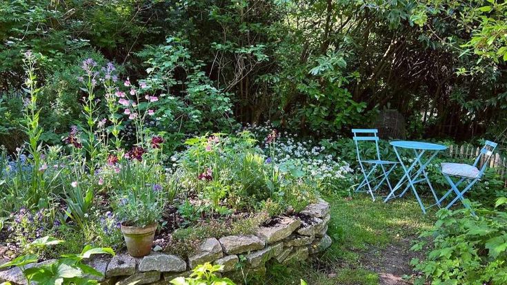 there is a chair and table in the garden next to each other with flowers growing around it