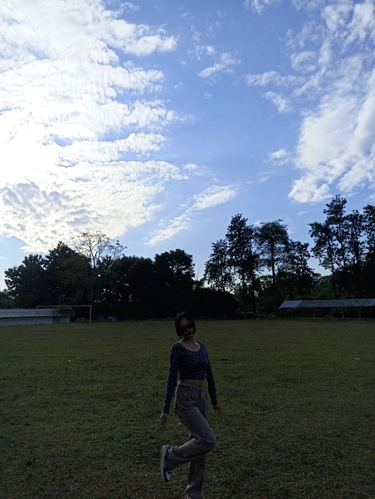 a woman standing on top of a lush green field under a blue sky with clouds