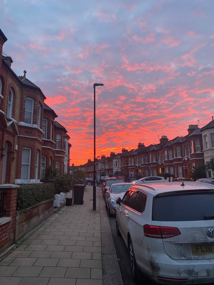 cars parked on the side of a street at sunset or dawn with pink clouds in the sky