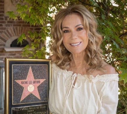 a woman holding a star on the hollywood walk of fame in front of a tree