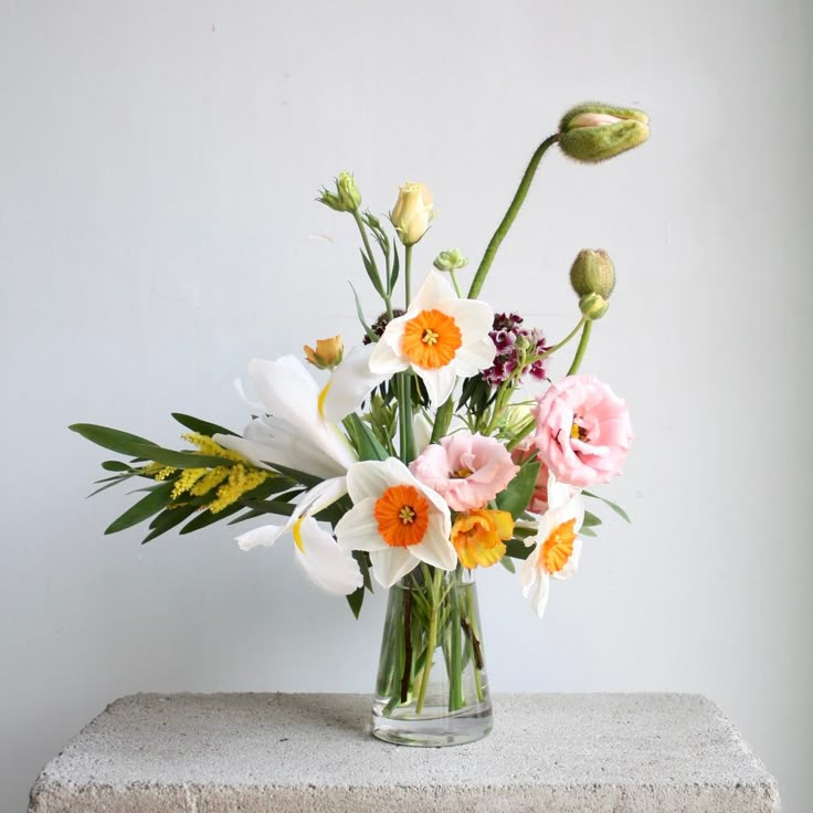 a vase filled with lots of flowers on top of a cement block next to a wall