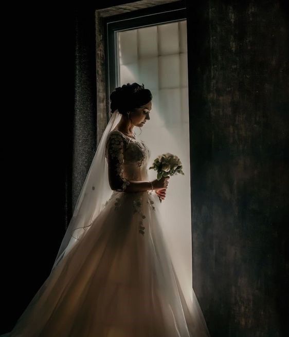 a woman in a wedding dress standing by a window