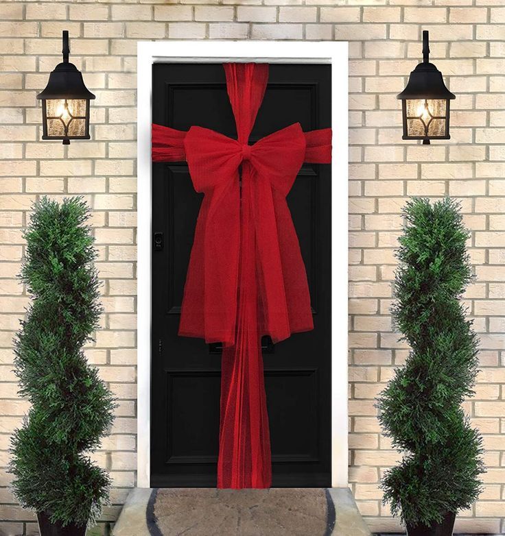 a red bow tied to the front door of a house with two potted plants