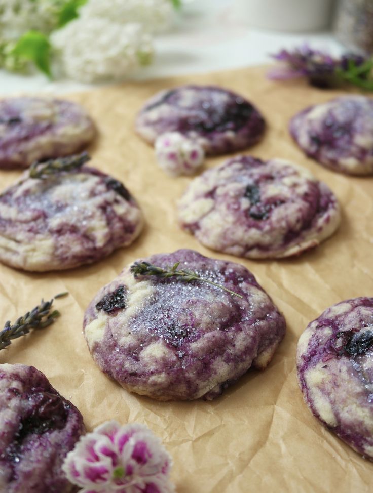 lavender cookies are arranged on a piece of wax paper with flowers in the background and greenery to the side