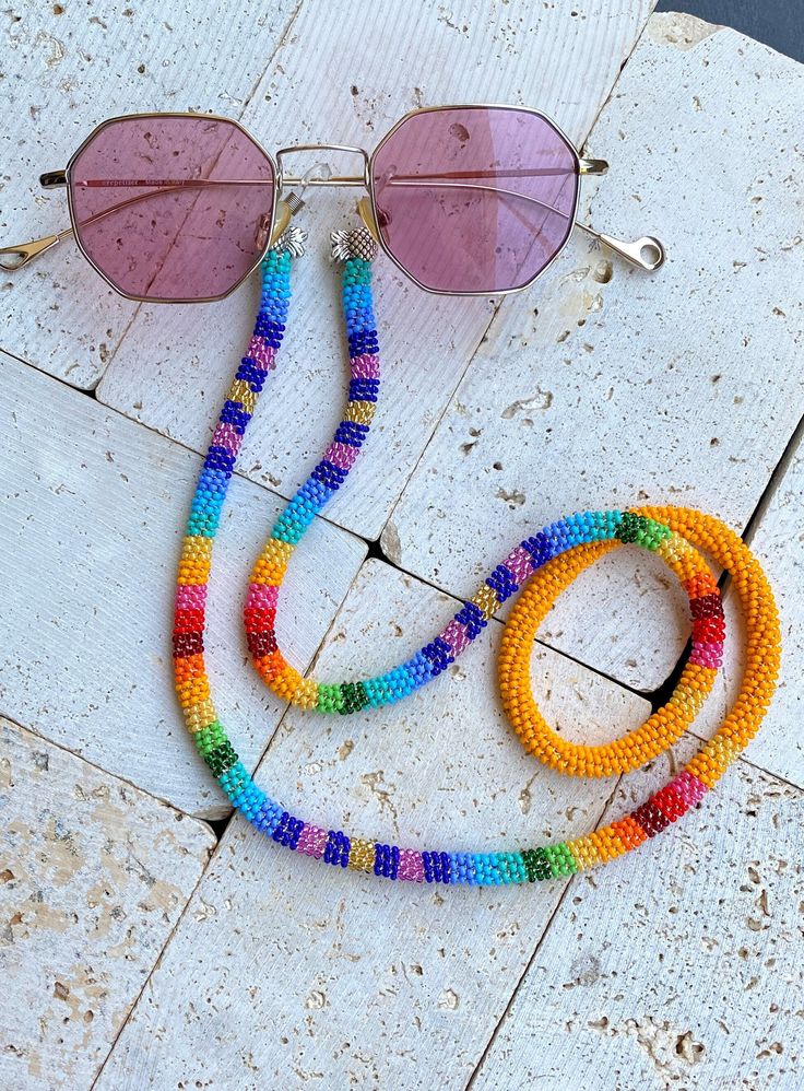 Handmade Beaded Sunglass Strap This sunglass strap is hand made is made out of beads with a very special prison bead technique.It has a tropical vibe with rainbow colours and stripe pattern which gives that contrast look with a tropical design feel. It can be worn in all seasons with all styles. Suitable for casual and occasional wearing. Great boho accessory for Summer and also for winter which beautifully compliments any outfit. The strap is 32 inch ( 81 cm)  long in total. The beaded part is 30 inches. It can fit all sunglass style's sized.  If you are looking for a unique gift this may be the right one for you as it is a rare find. Please do not hesitate to contact me if you have any questions. For other designs, please visit my shop LaPetiteidylleStore on Etsy: https://www.etsy.com/sh Eye Glass Holder, Sunglass Strap, Cute Anklets, Glasses Chains, Sunglasses Strap, Beaded Lanyard, Sunglass Chain, Beaded Lanyards, Rainbow Colours