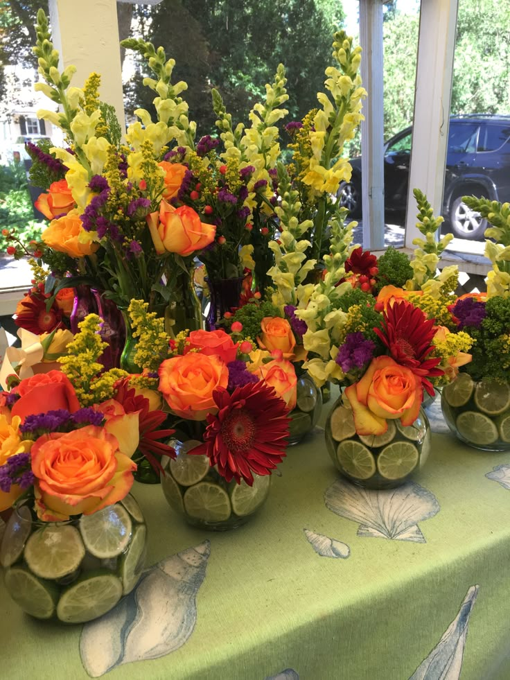 several vases filled with flowers sitting on top of a green tablecloth covered table