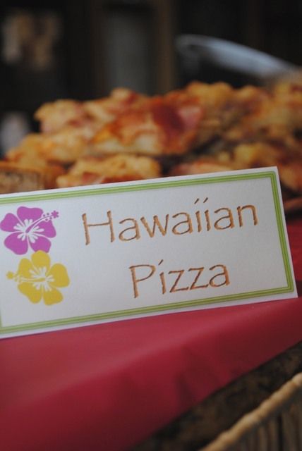 there is a sign that says hawaiian pizza on the table next to other food items