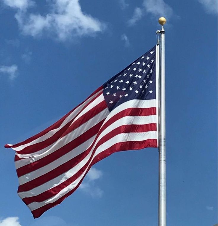 an american flag flying in the wind on a clear day with blue sky and clouds