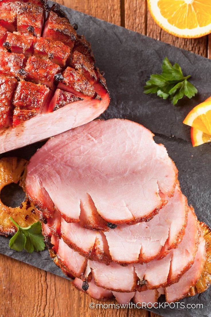 sliced ham on slate platter with oranges and parsley