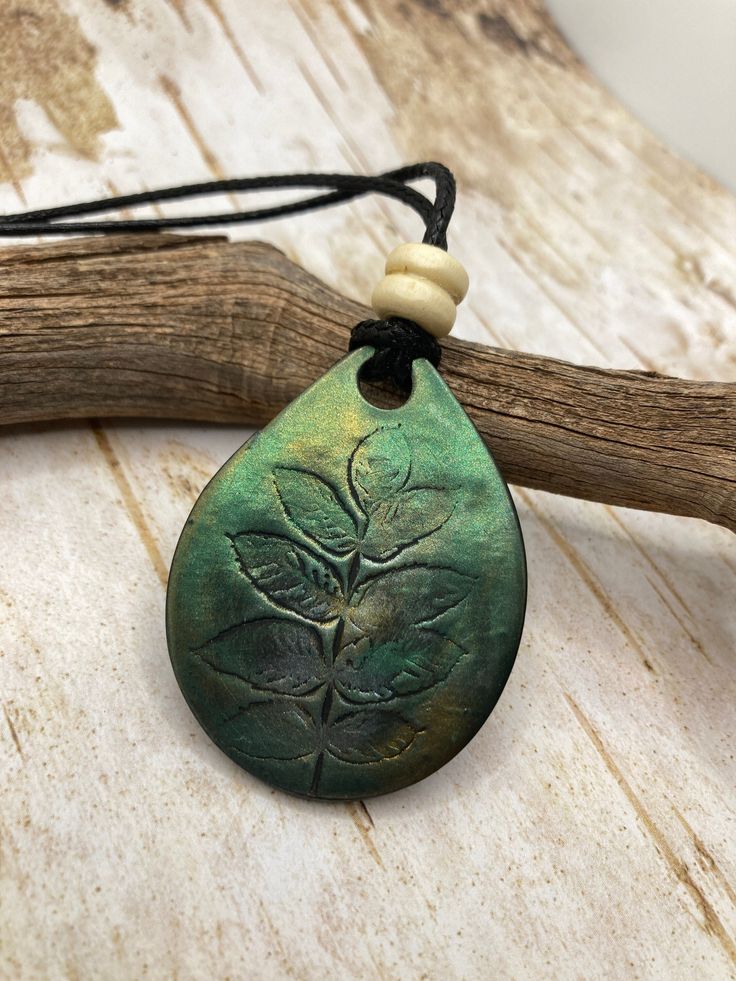 a green pendant with leaves on it sitting on top of a piece of drift wood