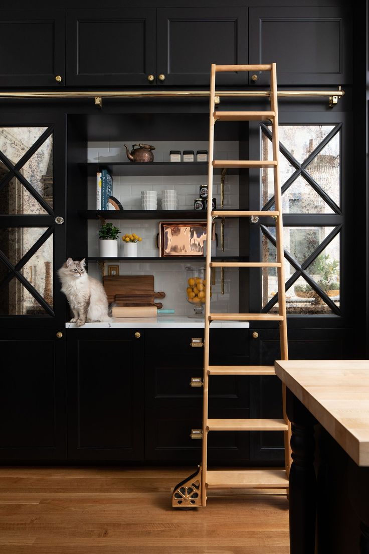 a cat sitting on top of a wooden step ladder in a kitchen next to a window