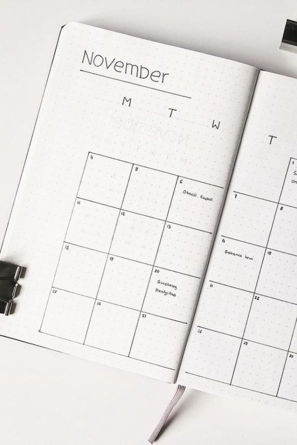 an open notebook with a calendar and pen on the page, next to it is a black ballpoint pen