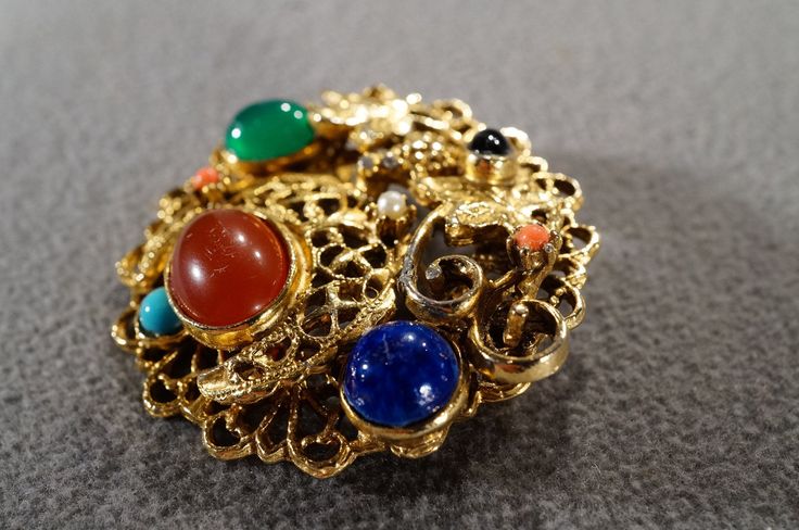 I am offering you this truly exquisite vintage classic spectacular very unique yellow gold tone tone pin brooch, with multi colored combination round and oval shaped bezel set faux turquoise, faux lapis,faux carnelian, faux coral,faux black onyx stone, faux pearl, and faux jade, in this marvelous dimensional domed round shaped design, just look at the marvelous colored rhinestones Very nice all prong set in a fancy scrolled raised relief etched scrolled yellow gold tone setting. What a spectacul Multicolor Round Brooch Jewelry, Vintage Gemstone Round Brooches, Vintage Multicolor Round Brooches, Oval Multi-stone Brooches As Gift, Vintage Multi-stone Yellow Gold Brooches, Vintage Yellow Gold Multi-stone Brooches, Vintage Multi-stone Brooches For Formal Occasions, Gold Multi-stone Brooch For Formal Occasions, Gold Multi-stone Brooches For Formal Occasions