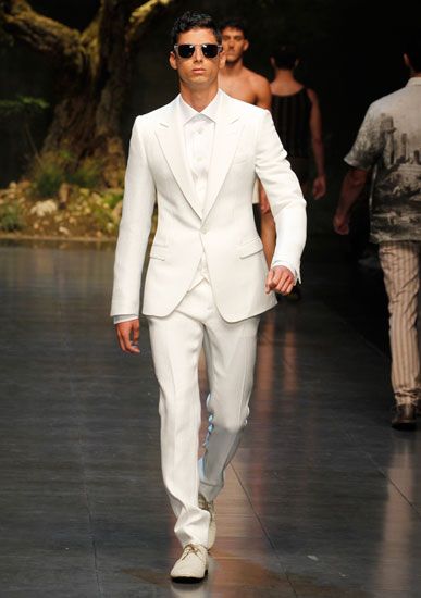 a man in a white suit and sunglasses walking down the runway at a fashion show