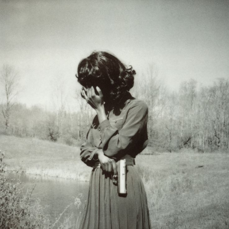 a woman standing in a field with her hand on her face while holding a bottle