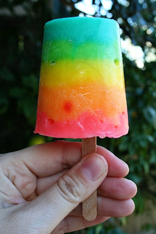 a hand holding a popsicle covered in rainbow colored ice cream