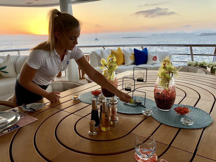 a woman is setting up drinks on the deck of a boat at sunset or dawn