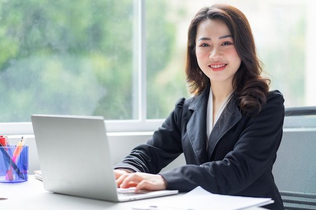 a woman sitting at a desk with a laptop computer in front of her, smiling