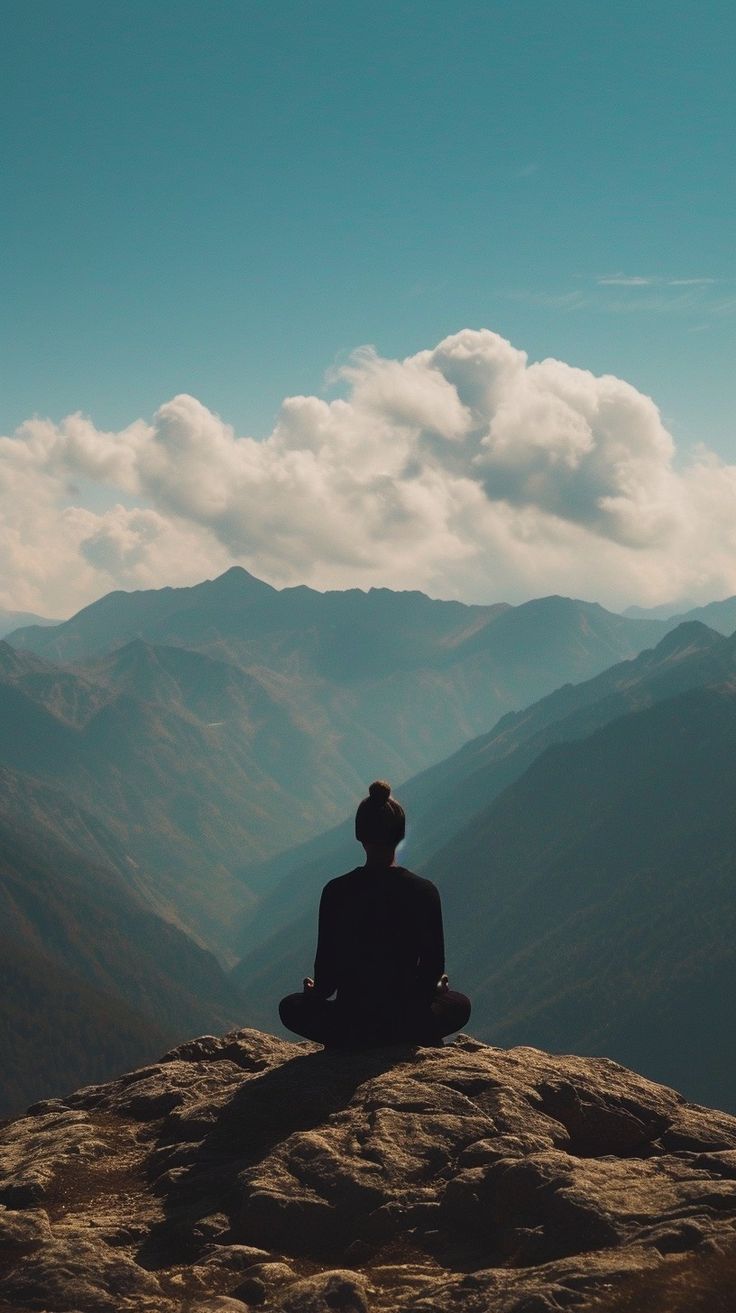 a person sitting on top of a mountain with mountains in the background and clouds in the sky