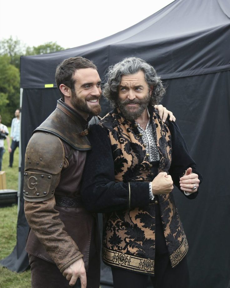 two men dressed in medieval clothing standing next to each other near a tented area