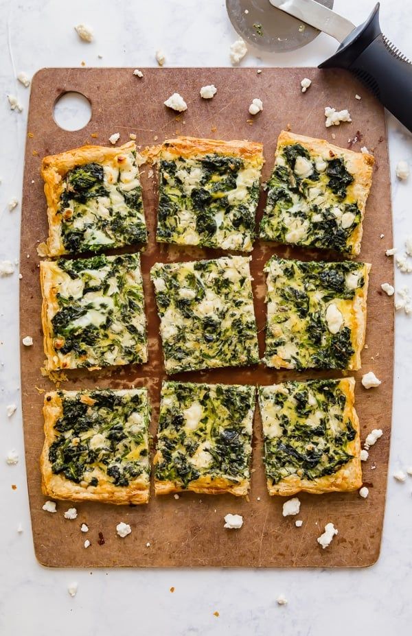 a cutting board topped with square slices of pizza covered in spinach and feta cheese