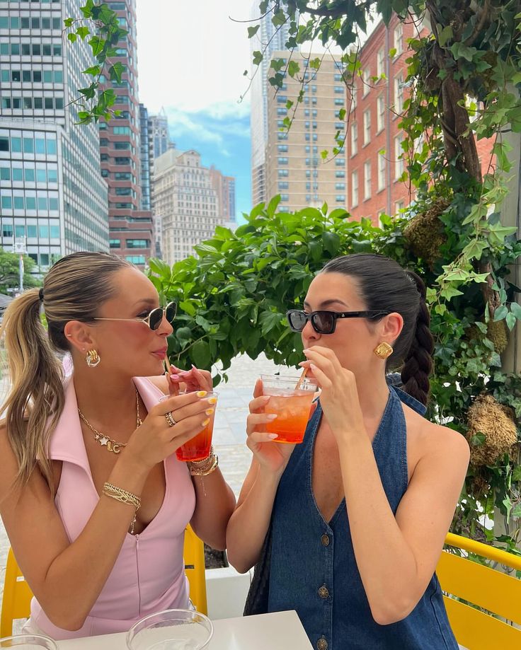 two women sitting at an outdoor table drinking cocktails and looking into each others eyes