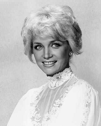 a black and white photo of a woman with blonde hair wearing a lace blouse, smiling at the camera